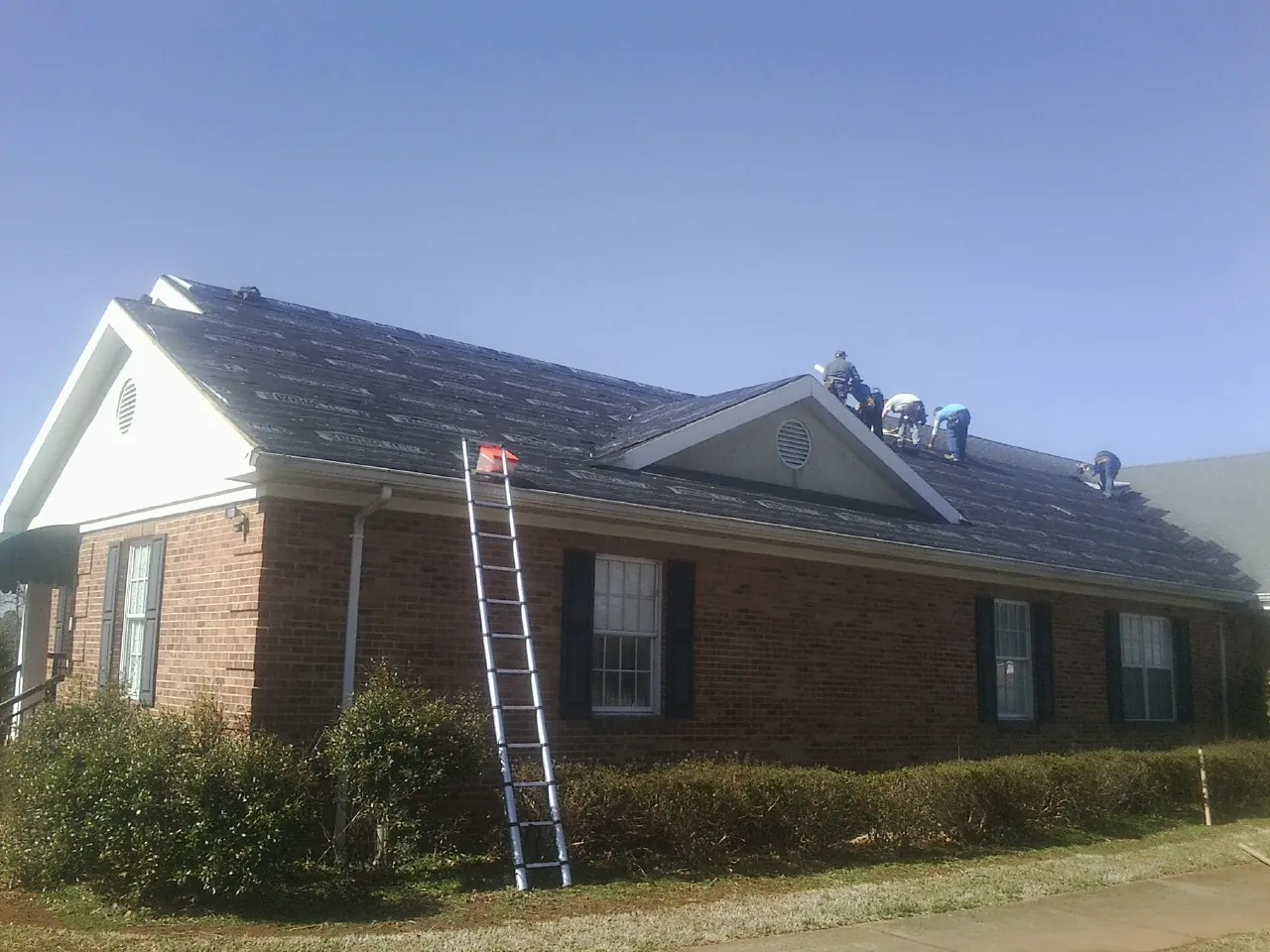 Crew tearing shingles off a brick ranch roof with a ladder set — Metal Roof Repair work by our crew in Saint George